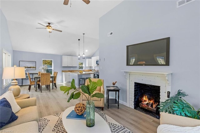 living room featuring light hardwood / wood-style flooring, a brick fireplace, high vaulted ceiling, and ceiling fan