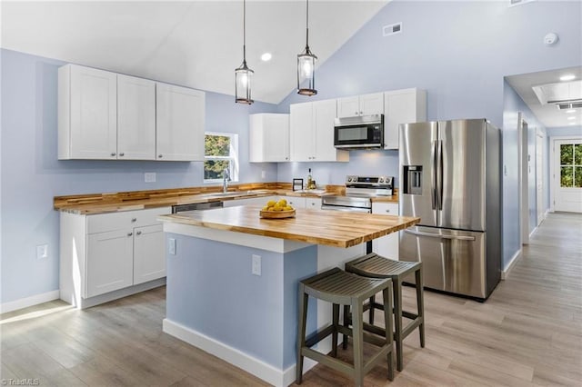 kitchen with hanging light fixtures, a kitchen island, appliances with stainless steel finishes, white cabinetry, and wood counters