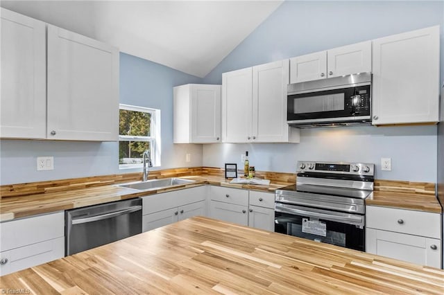 kitchen featuring butcher block counters, stainless steel appliances, vaulted ceiling, and white cabinets