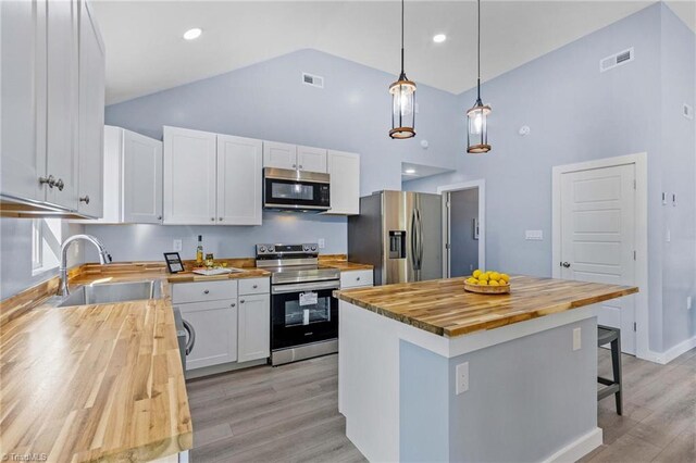 kitchen with white cabinets, stainless steel appliances, wood counters, and a kitchen island