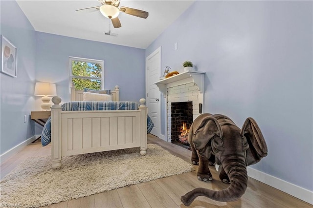 bedroom with light hardwood / wood-style floors, a brick fireplace, and ceiling fan