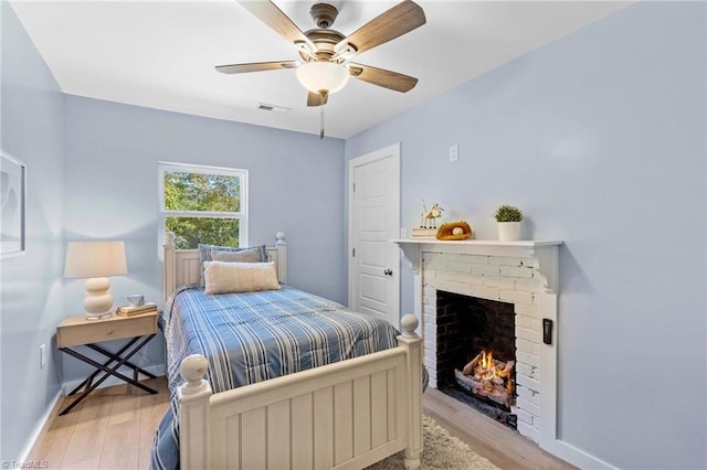 bedroom featuring a brick fireplace, light wood-type flooring, and ceiling fan