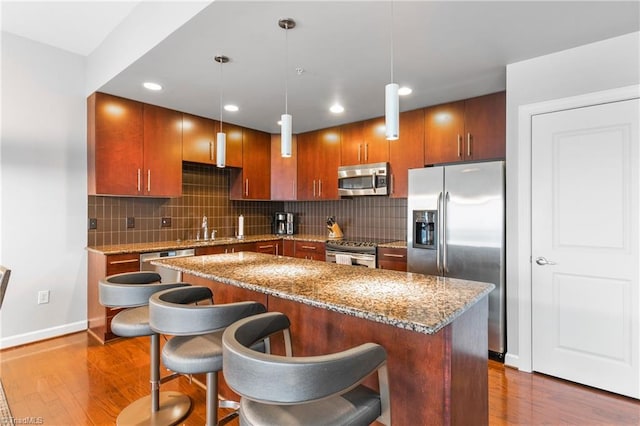 kitchen with hanging light fixtures, hardwood / wood-style floors, stainless steel appliances, sink, and decorative backsplash