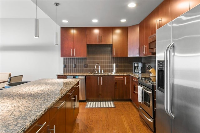 kitchen with backsplash, hanging light fixtures, light wood-type flooring, appliances with stainless steel finishes, and sink