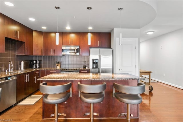 kitchen featuring light hardwood / wood-style flooring, appliances with stainless steel finishes, sink, pendant lighting, and tasteful backsplash