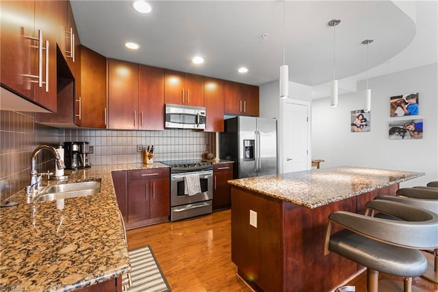 kitchen with light stone countertops, appliances with stainless steel finishes, light hardwood / wood-style floors, a breakfast bar, and sink