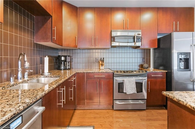 kitchen with tasteful backsplash, stainless steel appliances, sink, light stone countertops, and light hardwood / wood-style floors