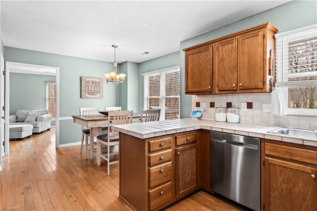 kitchen with stainless steel dishwasher, tile countertops, kitchen peninsula, and hanging light fixtures