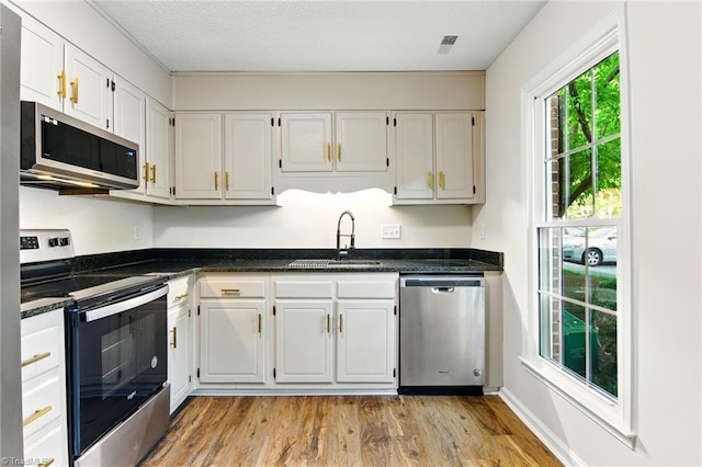 3985 Valley Ct Unit B, Winston-Salem, NC 27106 - kitchen featuring appliances with stainless steel finishes, a sink, light wood-style flooring, white cabinetry, and dark stone counters
