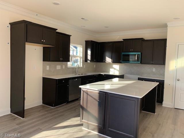 kitchen featuring dishwasher, a kitchen island, stainless steel microwave, light wood-type flooring, and a sink