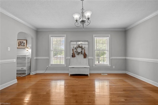 unfurnished dining area with a chandelier, hardwood / wood-style floors, a textured ceiling, arched walkways, and baseboards