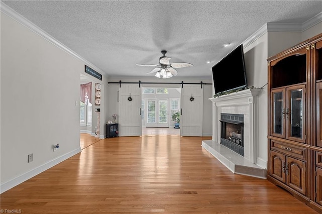 unfurnished living room featuring a barn door, a textured ceiling, light wood-style flooring, crown molding, and ceiling fan
