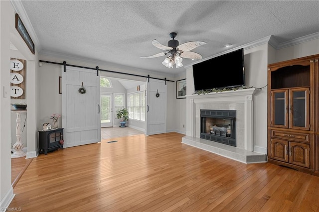 unfurnished living room featuring a barn door, light wood-style flooring, a ceiling fan, a textured ceiling, and ornamental molding