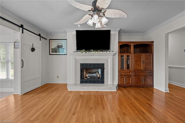 unfurnished living room with a textured ceiling, ceiling fan, wood finished floors, a barn door, and baseboards