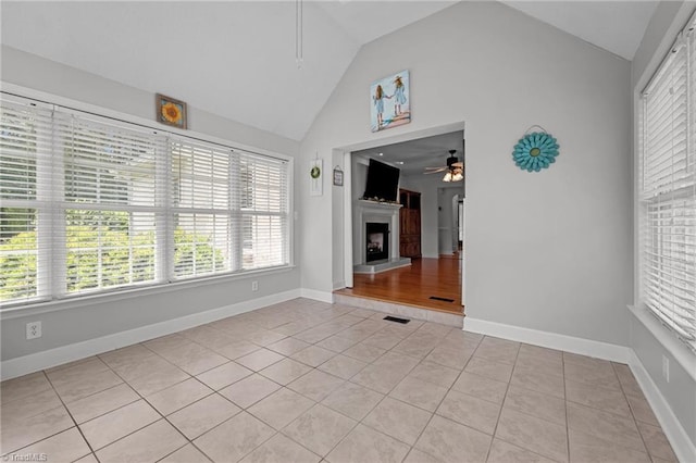 unfurnished living room featuring ceiling fan, light tile patterned floors, plenty of natural light, a fireplace with raised hearth, and high vaulted ceiling