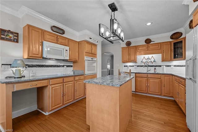 kitchen featuring white appliances, arched walkways, a sink, tasteful backsplash, and a center island