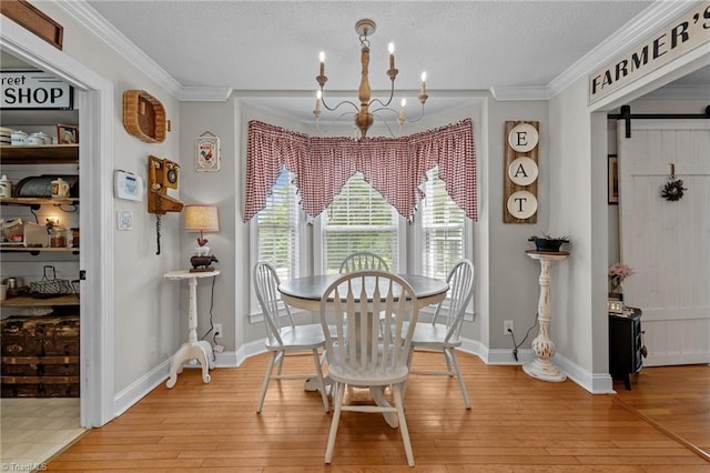 dining room with a chandelier, light wood-style flooring, a barn door, ornamental molding, and a textured ceiling
