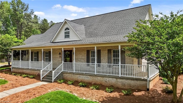 farmhouse featuring a porch, roof with shingles, and brick siding