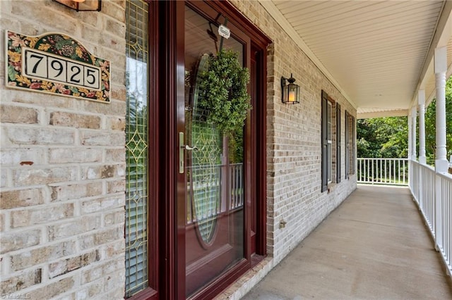 view of exterior entry featuring covered porch and brick siding