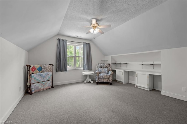 living area featuring carpet flooring, ceiling fan, vaulted ceiling, a textured ceiling, and baseboards