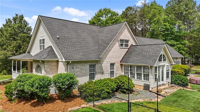 rear view of house featuring roof with shingles, brick siding, a sunroom, and a lawn