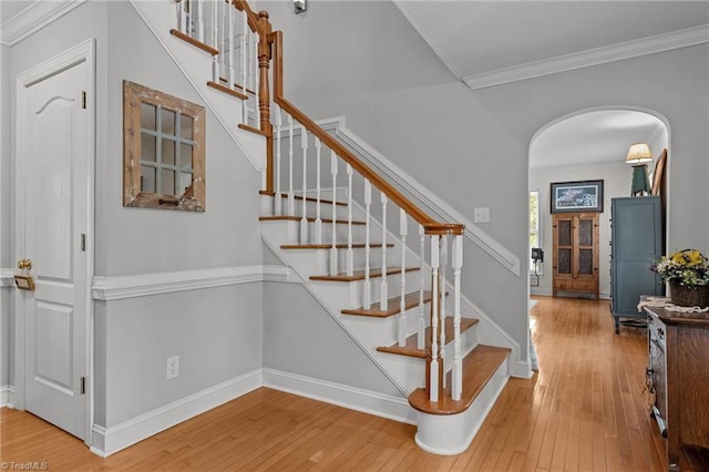 staircase featuring arched walkways, hardwood / wood-style floors, crown molding, and baseboards