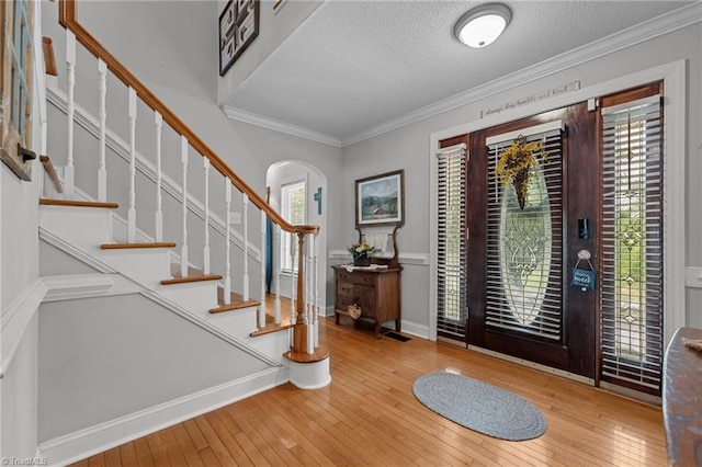 foyer featuring arched walkways, wood-type flooring, stairs, ornamental molding, and a textured ceiling