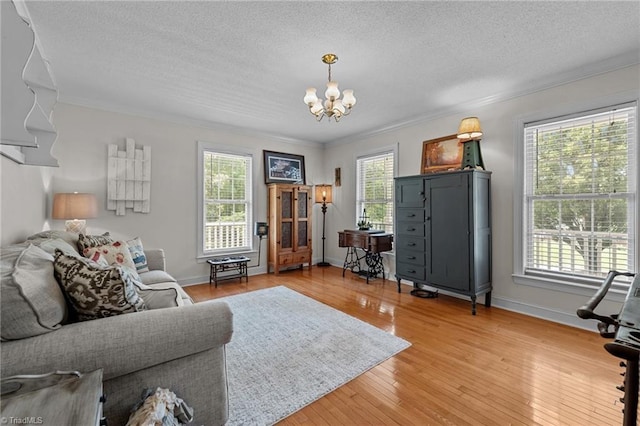 living area with a chandelier, a textured ceiling, ornamental molding, light wood-type flooring, and baseboards