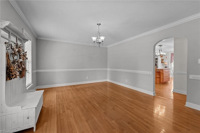 unfurnished dining area with a chandelier, arched walkways, light wood-type flooring, baseboards, and ornamental molding