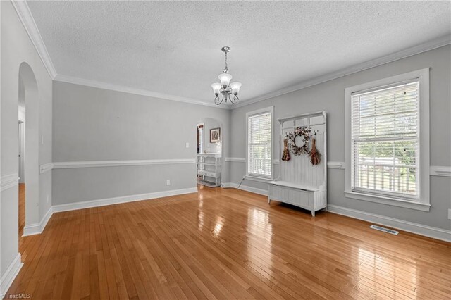 unfurnished dining area with arched walkways, a textured ceiling, a chandelier, hardwood / wood-style flooring, and ornamental molding