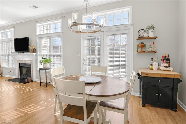 dining area featuring baseboards, visible vents, a fireplace, light wood-style floors, and crown molding