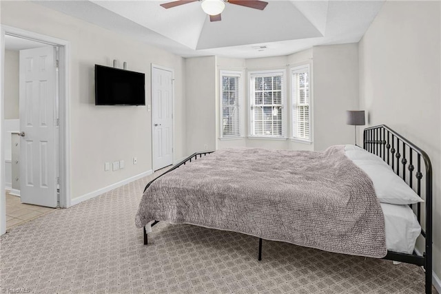 bedroom featuring a raised ceiling, carpet, baseboards, and ceiling fan