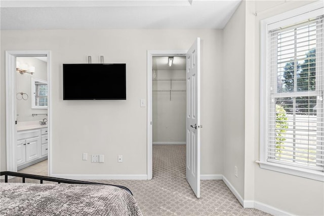 bedroom featuring light carpet, ensuite bath, a closet, baseboards, and a spacious closet