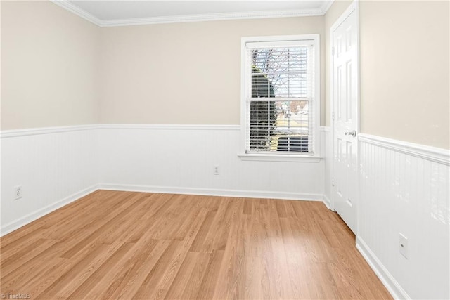 empty room with crown molding, light wood-style floors, and wainscoting