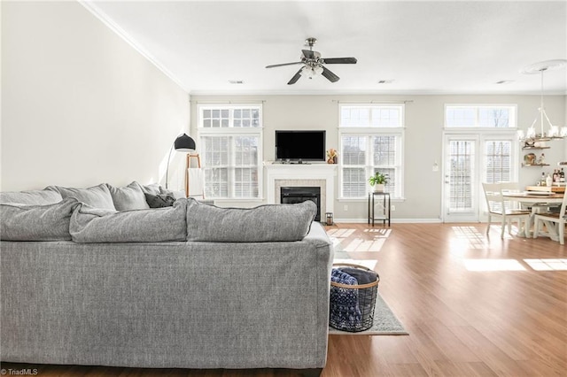 living room featuring baseboards, ornamental molding, ceiling fan with notable chandelier, a tile fireplace, and wood finished floors