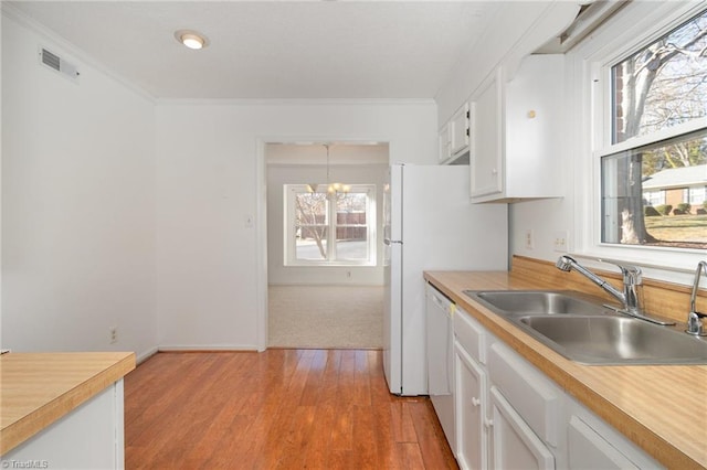 kitchen with sink, ornamental molding, white cabinets, decorative light fixtures, and light wood-type flooring