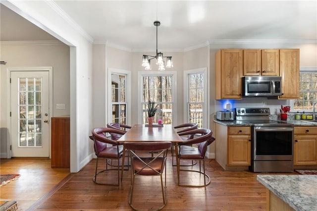 kitchen with an inviting chandelier, appliances with stainless steel finishes, ornamental molding, and light wood finished floors