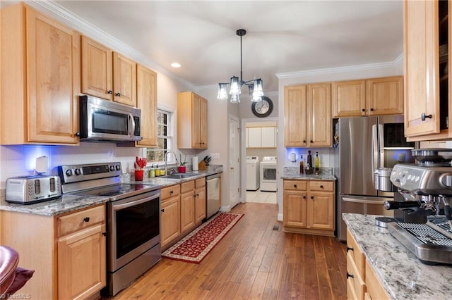 kitchen featuring washing machine and clothes dryer, crown molding, hardwood / wood-style floors, appliances with stainless steel finishes, and a sink