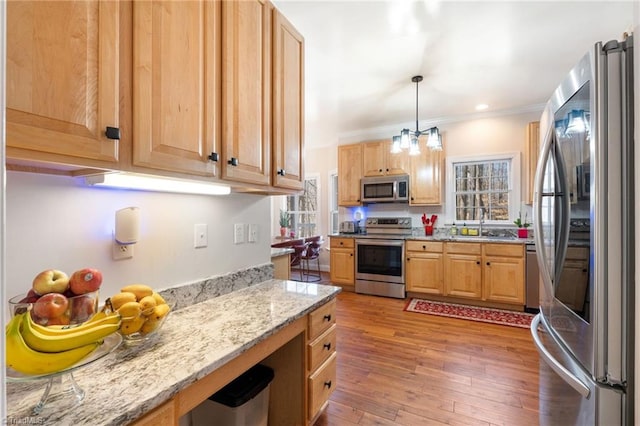 kitchen featuring light stone countertops, a sink, ornamental molding, hardwood / wood-style flooring, and appliances with stainless steel finishes