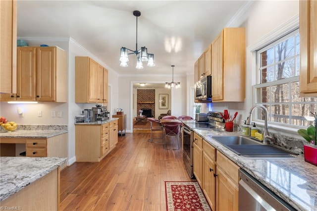 kitchen with light wood-style flooring, light brown cabinetry, a sink, appliances with stainless steel finishes, and a fireplace