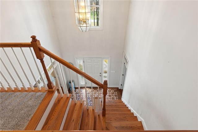 stairway with baseboards, a high ceiling, an inviting chandelier, and wood finished floors