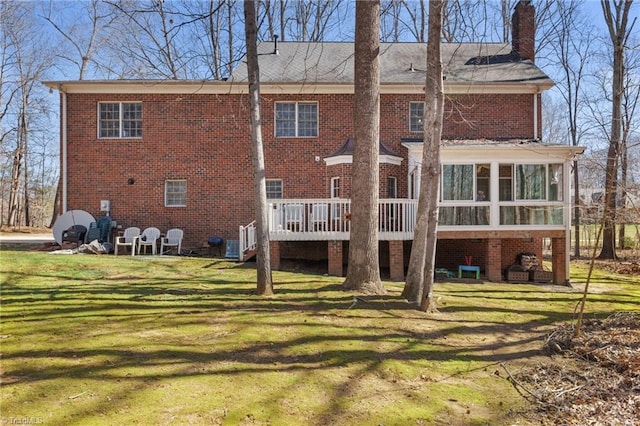 back of property featuring a deck, a yard, a sunroom, brick siding, and a chimney