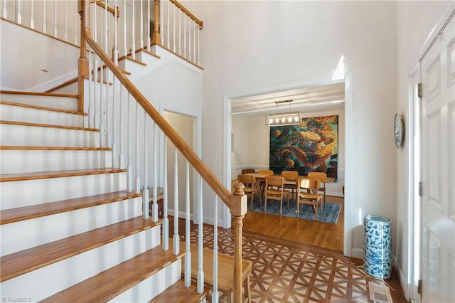 staircase with visible vents, a high ceiling, baseboards, and wood finished floors