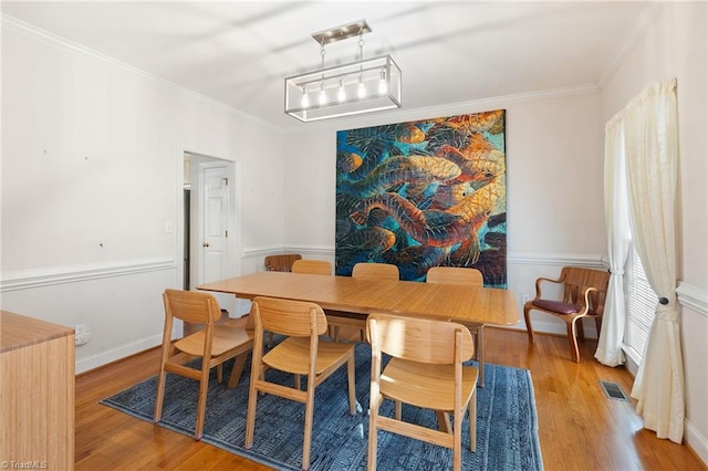 dining area with visible vents, baseboards, wood finished floors, and ornamental molding