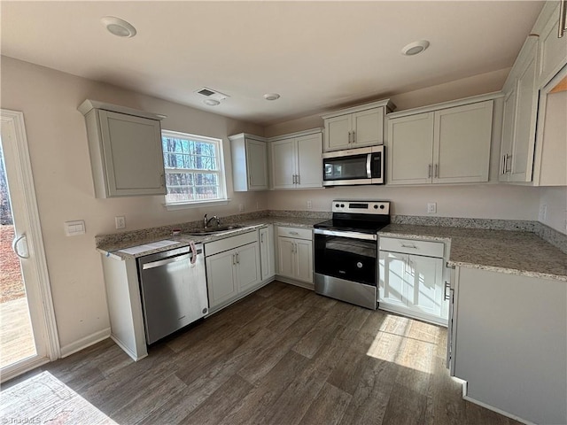 kitchen with sink, light stone counters, appliances with stainless steel finishes, dark hardwood / wood-style flooring, and white cabinets