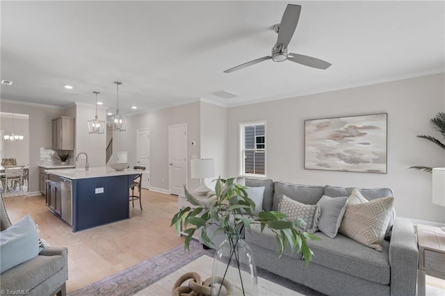 living room with ceiling fan with notable chandelier, ornamental molding, baseboards, and light wood-style floors