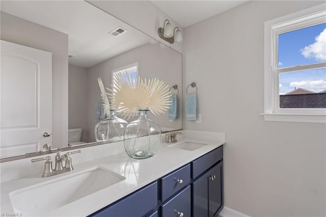 bathroom with toilet, double vanity, a sink, and visible vents