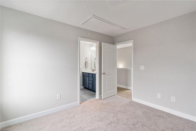 unfurnished bedroom with attic access, light colored carpet, baseboards, and ensuite bathroom