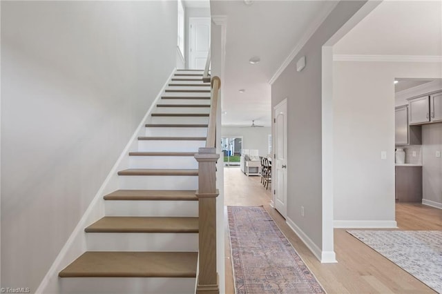 stairs with a ceiling fan, crown molding, baseboards, and wood finished floors