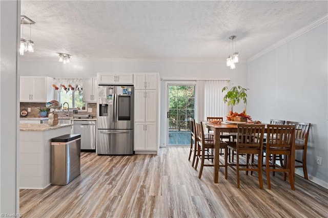 dining room with ornamental molding, light wood-type flooring, a textured ceiling, and a wealth of natural light